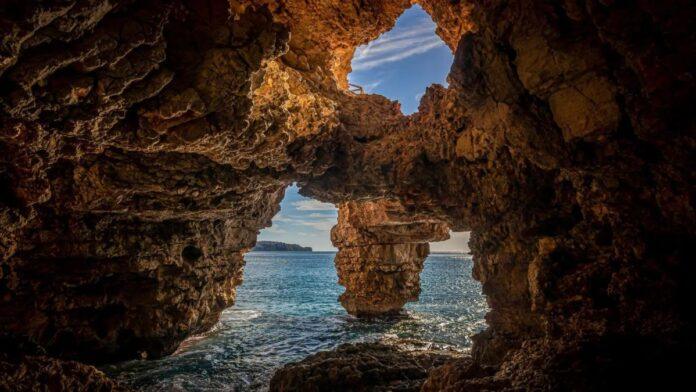 Entrada de la Cueva de la Marina Grande en Alicante, formaciones rocosas naturales junto al mar Mediterráneo en un día soleado.
