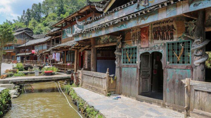 Aldea Huanggang en Guizhou, China, con casas tradicionales de madera del pueblo Dong junto a un canal